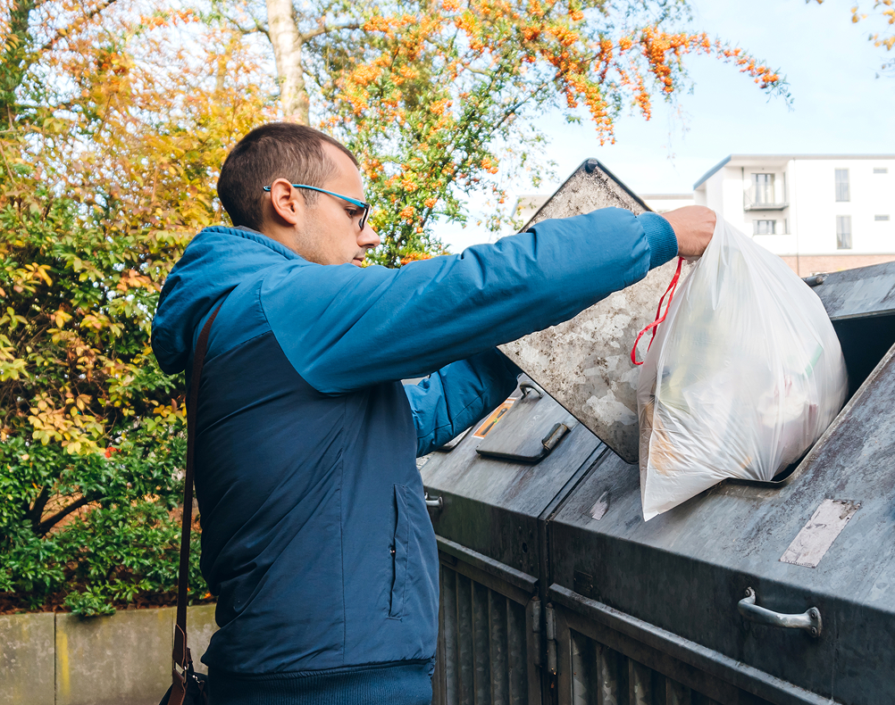 GettyImages-1172201558 1 Man disposing of trash in outdoor bin.